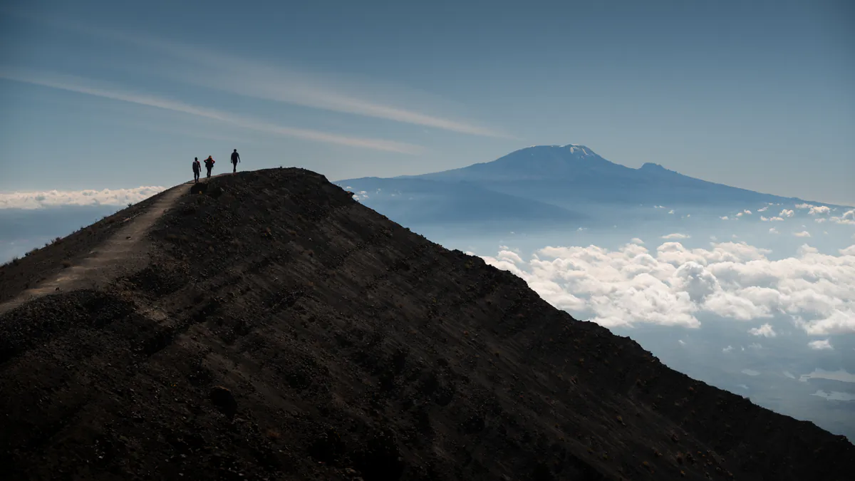 Hikers on a Mount Meru ridge with Kilimanjaro above the clouds